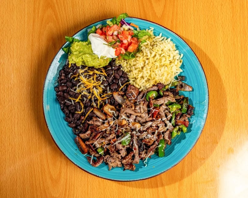 A vibrant Mexican dish with steak, rice, black beans, guacamole, pico de gallo, and salad.