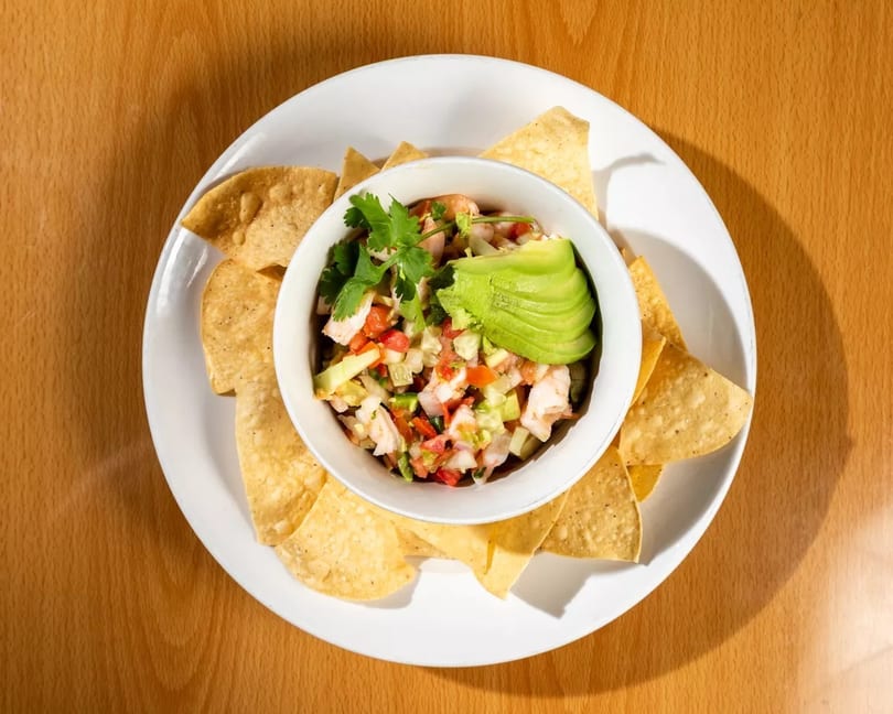A bowl of fresh shrimp ceviche with avocado and cilantro, surrounded by tortilla chips.