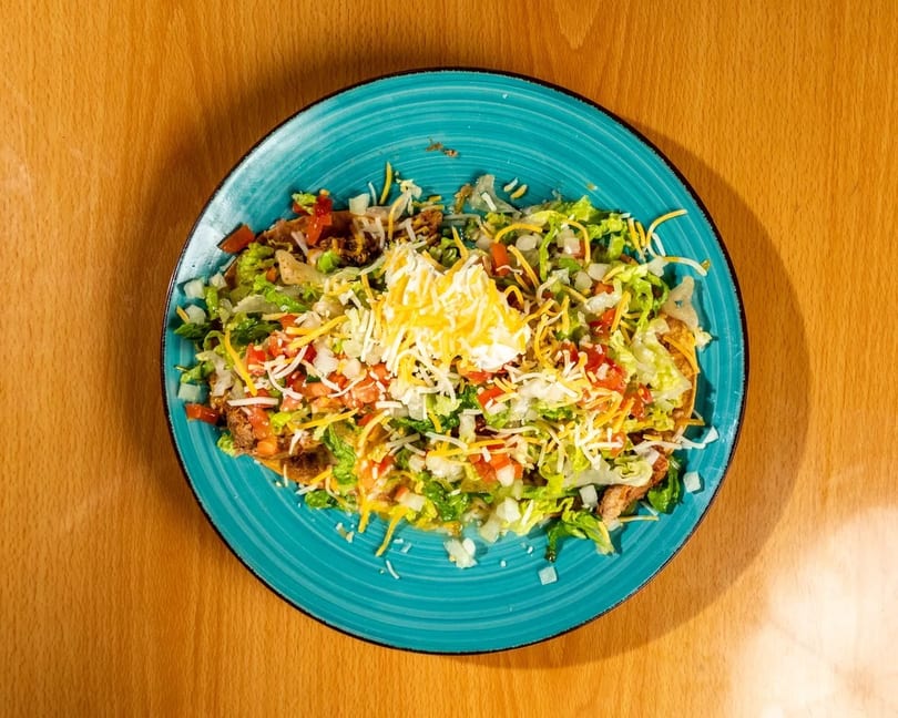 Overhead view of a taco salad with lettuce, tomatoes, cheese, and sour cream on a blue plate.
